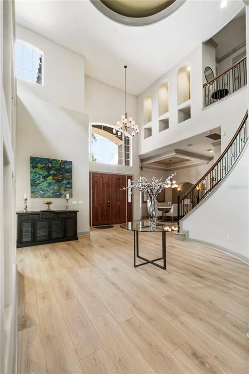 A grand foyer features light wood flooring, a curved staircase, and a high ceiling — 7926 VERSILIA DRIVE, ORLANDO, FL