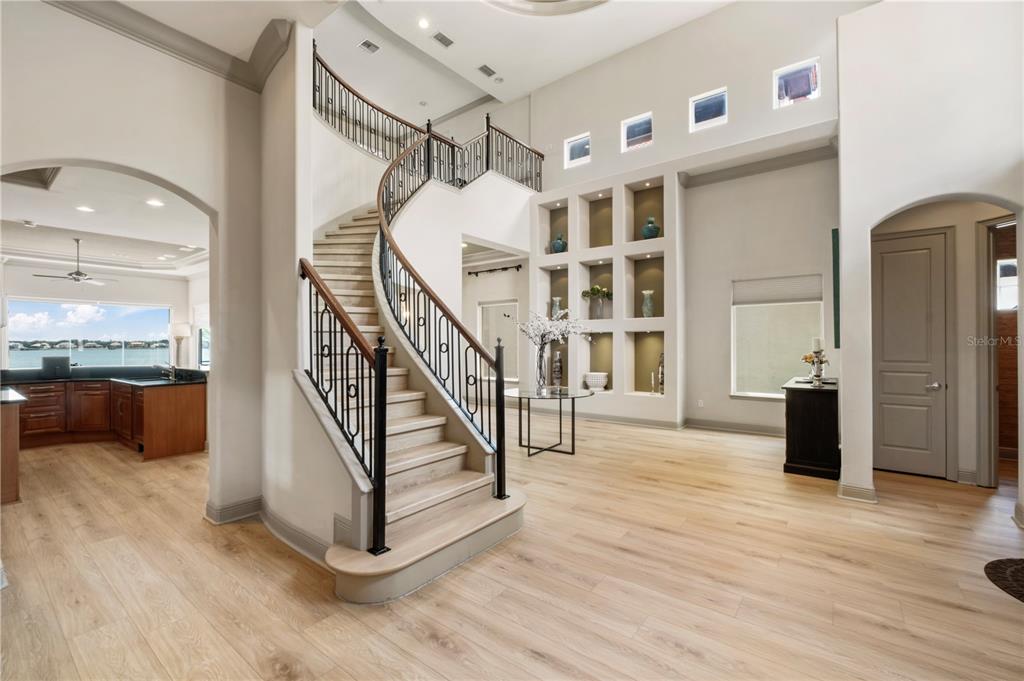 A grand foyer features a curved staircase with iron railings and light wood flooring — 7926 VERSILIA DRIVE, ORLANDO, FL