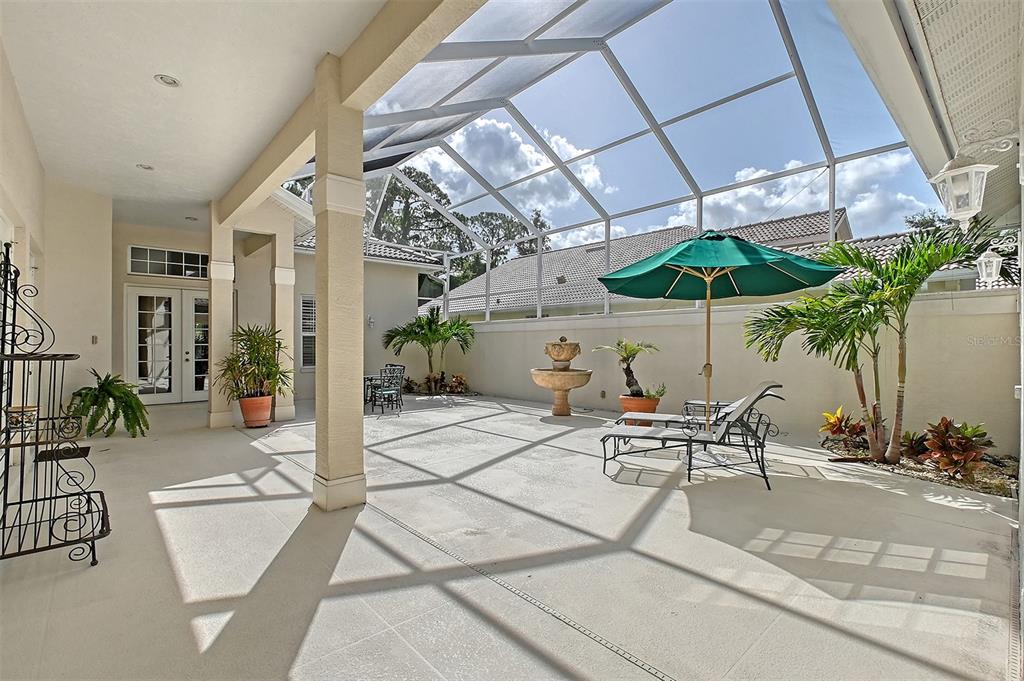 A screened-in patio features a concrete floor, a fountain, lounge chairs, and a green umbrella — 5839 LOS VERDES COURT, BRADENTON, FL