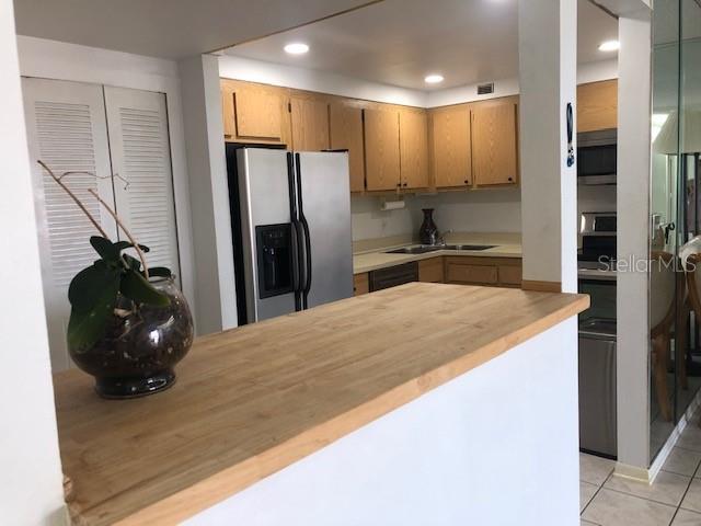 A kitchen features light wood cabinets, a stainless steel refrigerator, and a wooden breakfast bar — 830 S GULFVIEW BOULEVARD UNIT 601, CLEARWATER BEACH, FL
