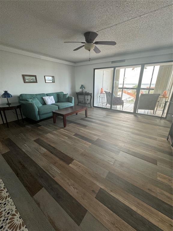 A living room features a teal sofa, wood-look flooring, a ceiling fan, and a balcony view — 830 S GULFVIEW BOULEVARD UNIT 601, CLEARWATER BEACH, FL