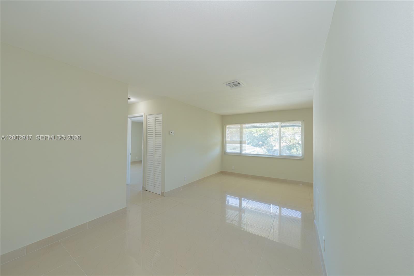 An empty room features light-colored tile flooring, white walls, and a large window — 939 Magnolia DRIVE # L, Lake Park FL 33403, LAKE PARK, FL