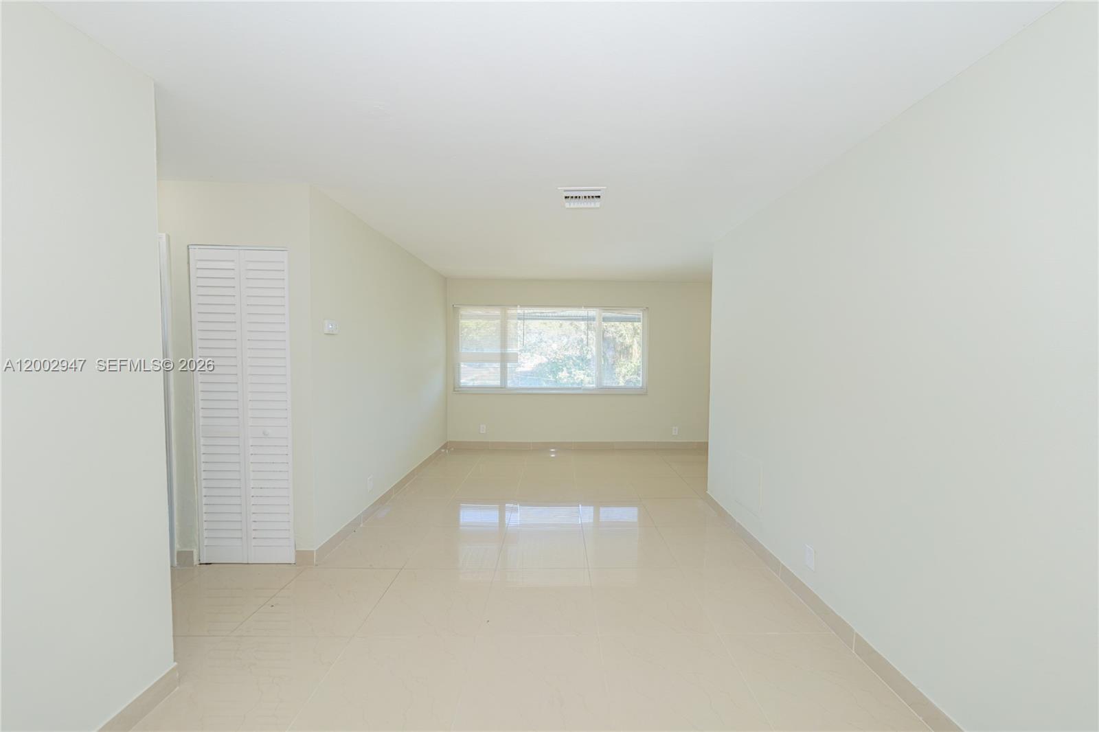 An empty room features light-colored tile flooring, white walls, and a large window — 939 Magnolia DRIVE # L, Lake Park FL 33403, LAKE PARK, FL