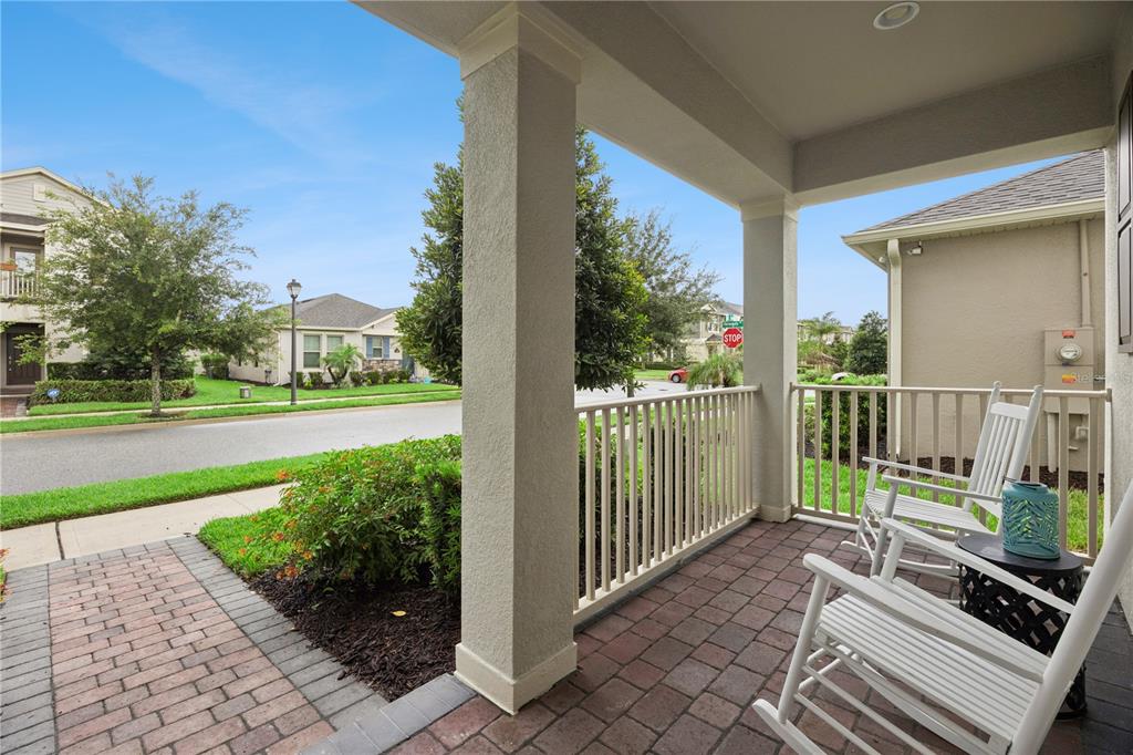 A covered front porch with brick pavers, white railings, and two white rocking chairs — 9462 KOMIKA LANE, WINTER GARDEN, FL