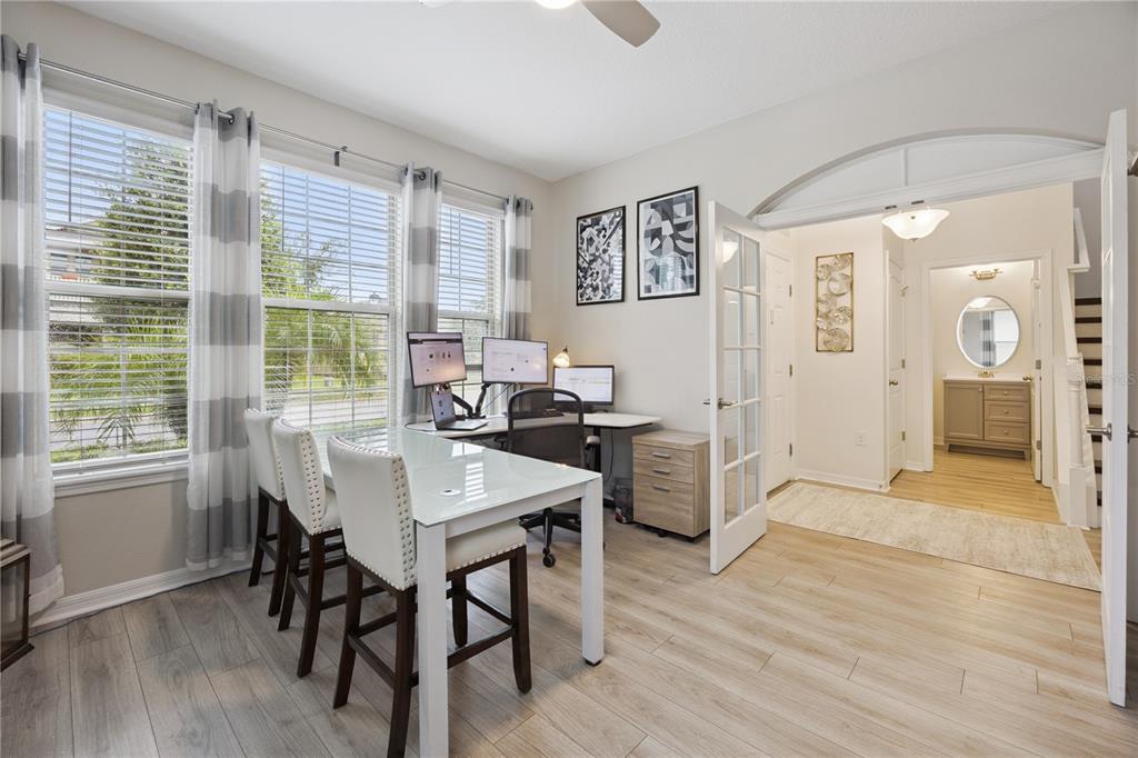 A home office with a glass desk, multiple monitors, and French doors leading to a hallway — 9462 KOMIKA LANE, WINTER GARDEN, FL