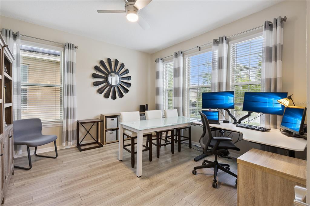 A home office features a desk with multiple monitors, a dining table, and wood flooring — 9462 KOMIKA LANE, WINTER GARDEN, FL