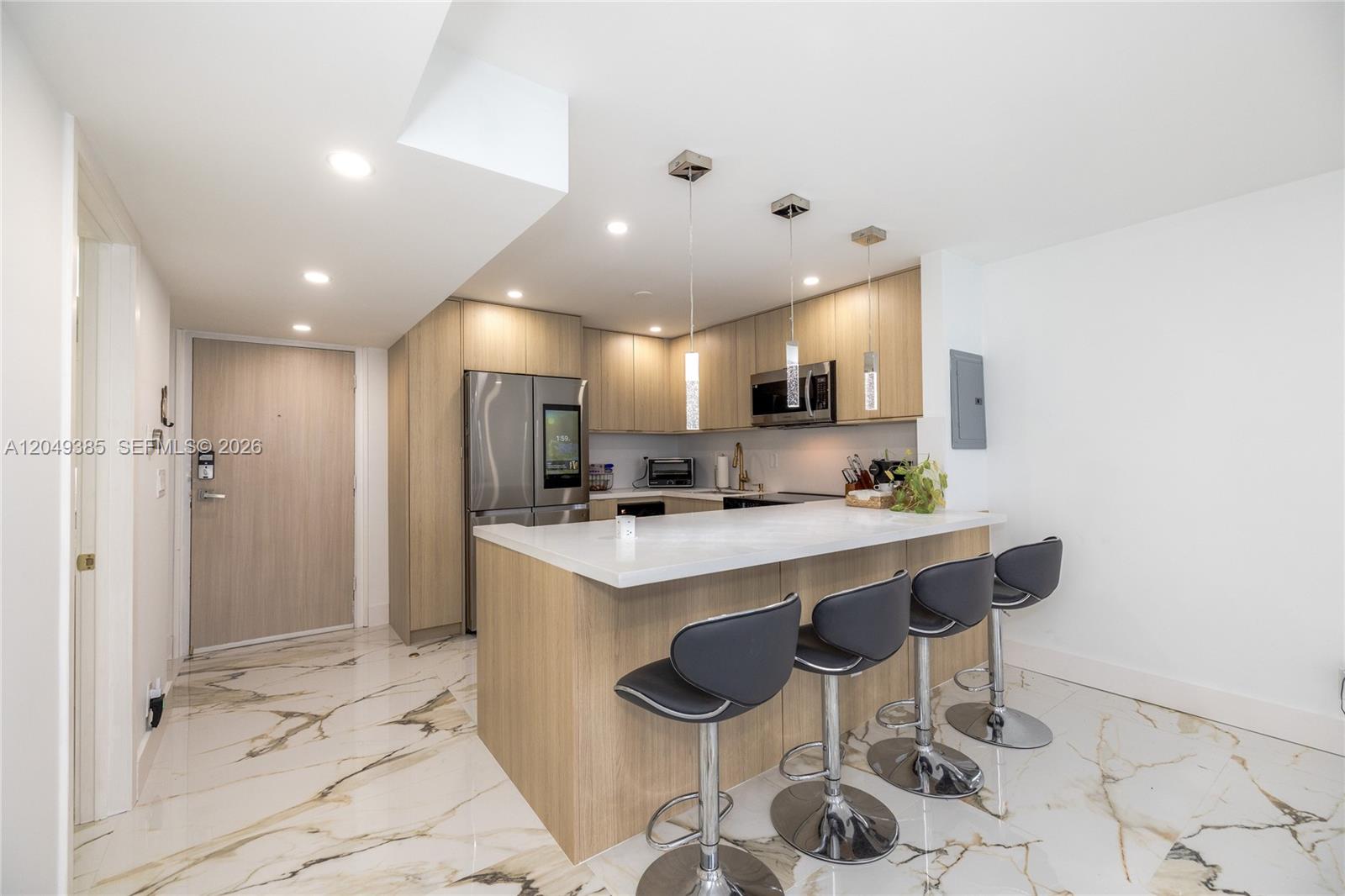 A modern kitchen features light wood cabinetry, a white countertop island, and marble-patterned tile flooring — 400 N Surf # 1002, Hollywood FL 33019, HOLLYWOOD, FL