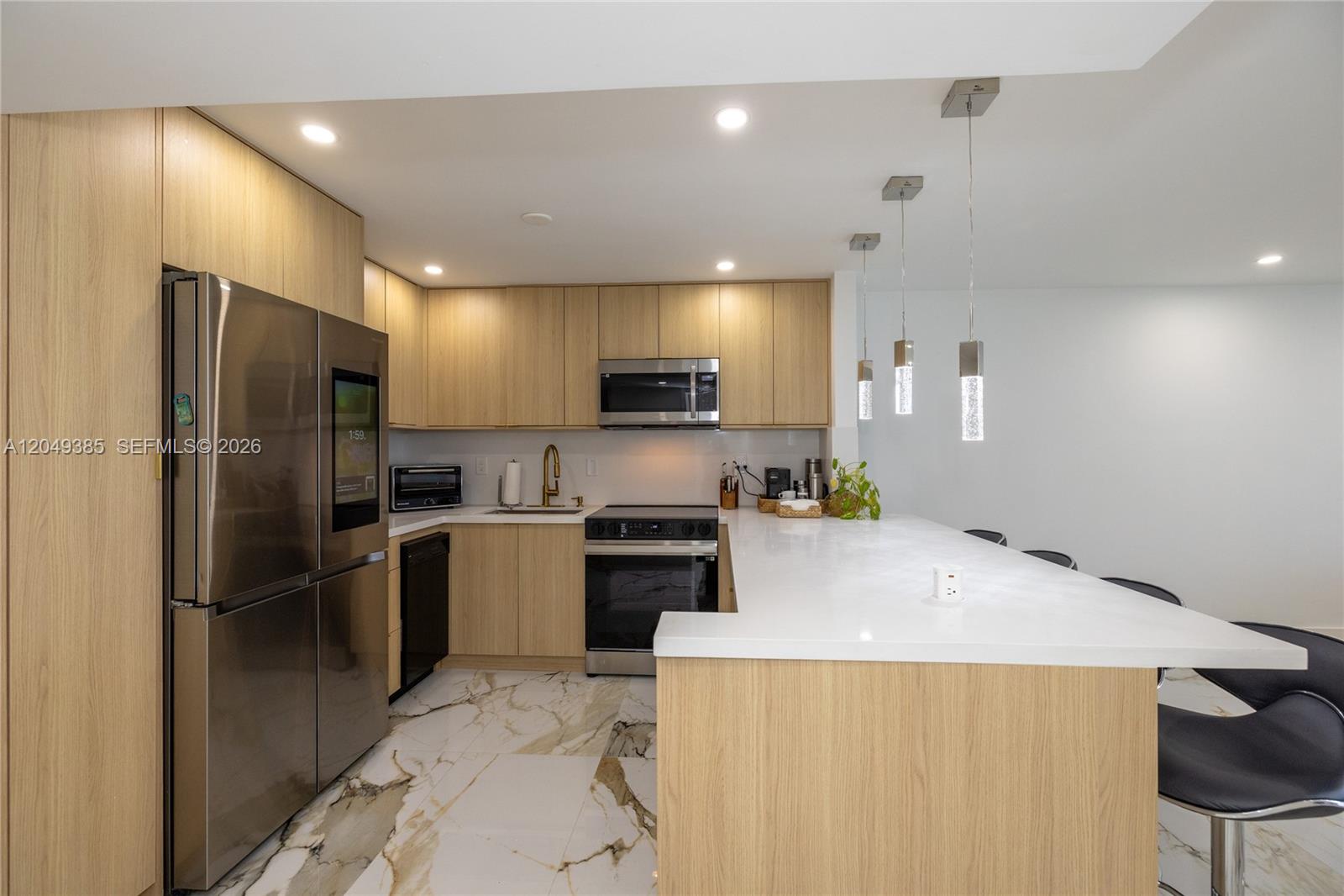 A modern kitchen features light wood cabinetry, white countertops, and marble-patterned tile flooring — 400 N Surf # 1002, Hollywood FL 33019, HOLLYWOOD, FL