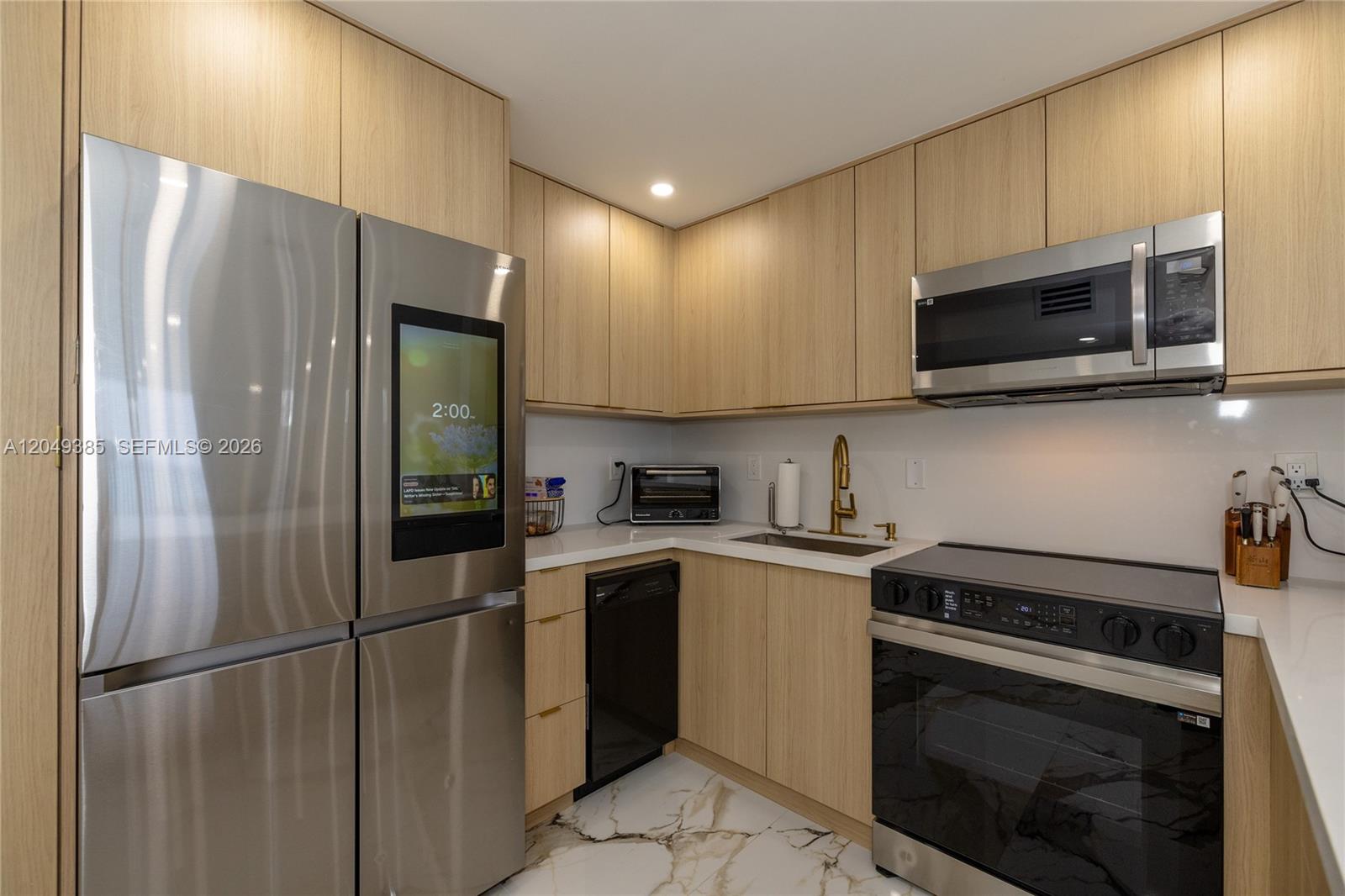 A modern kitchen features light wood cabinetry, stainless steel appliances, and white marble-patterned flooring — 400 N Surf # 1002, Hollywood FL 33019, HOLLYWOOD, FL