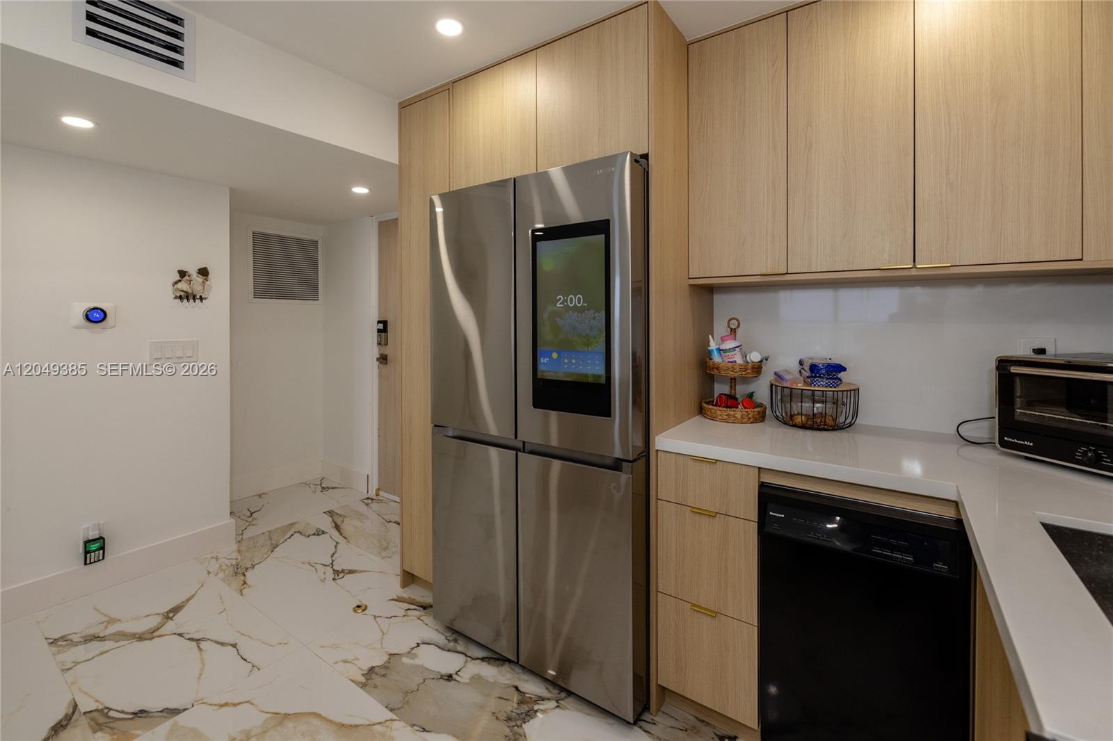 A modern kitchen features light wood cabinetry, a smart refrigerator, and white marble-patterned tile flooring — 400 N Surf # 1002, Hollywood FL 33019, HOLLYWOOD, FL