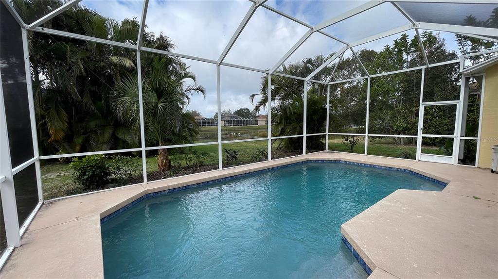 A screened-in swimming pool sits on a concrete patio overlooking a grassy backyard — 210 41ST STREET NE, BRADENTON, FL