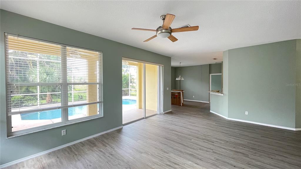 An empty living room features light green walls, wood-look flooring, a ceiling fan, and pool views — 210 41ST STREET NE, BRADENTON, FL