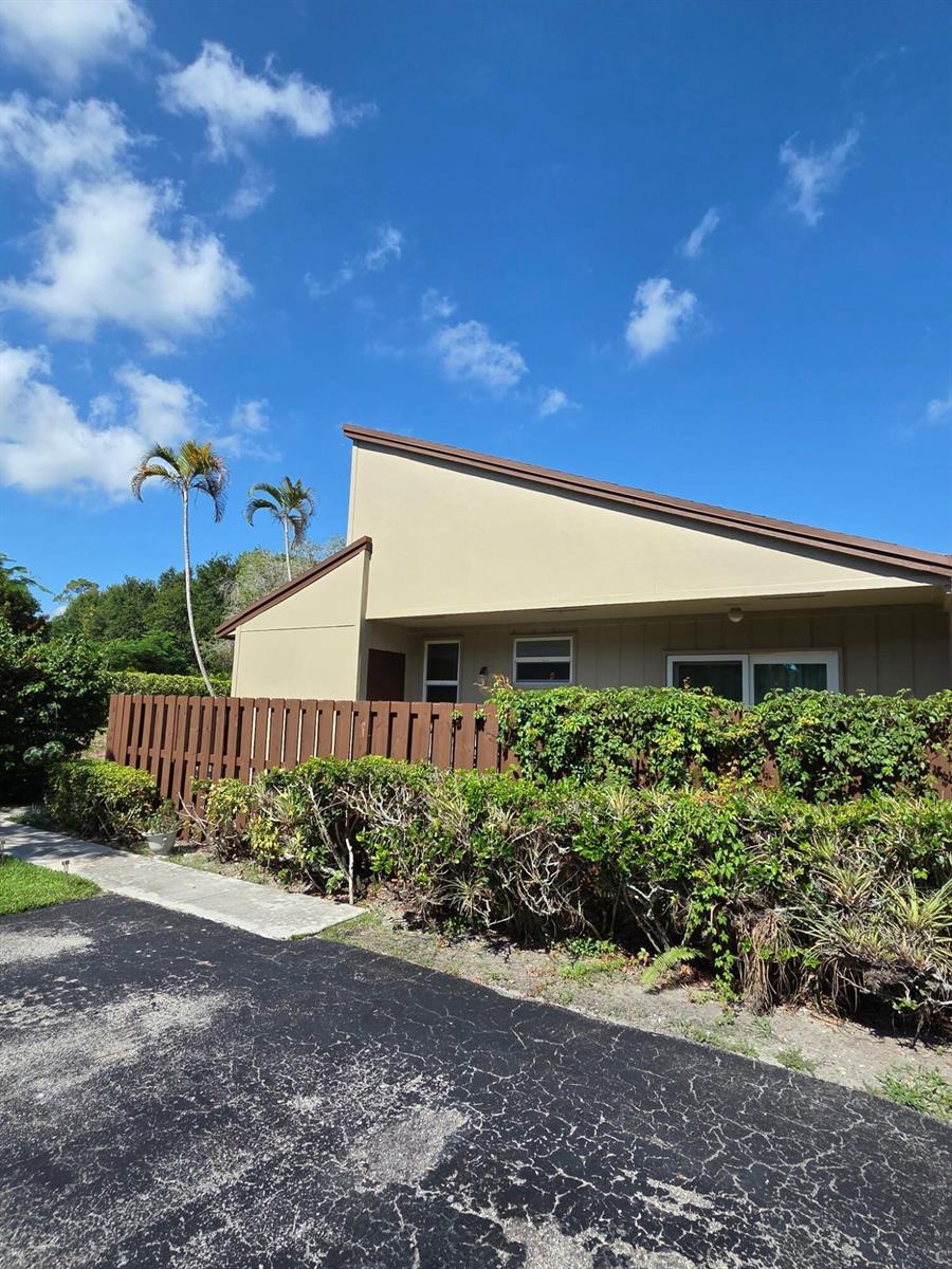 A tan, single-story house with a slanted roof sits behind a brown wooden fence — 11600 Timbers Way # 37a, Boca Raton FL 33428, BOCA RATON, FL