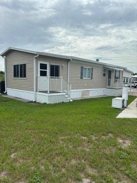 A tan mobile home with white skirting and a small front porch sits on grass — 9000 US HWY 192 UNIT 56, CLERMONT, FL