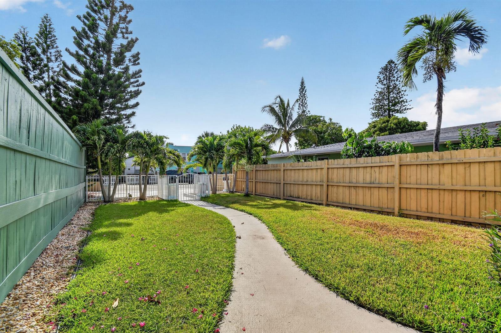 A backyard features a concrete path, green lawn, palm trees, and wooden privacy fencing — 508 N K Street # 1, FL 33460, FL
