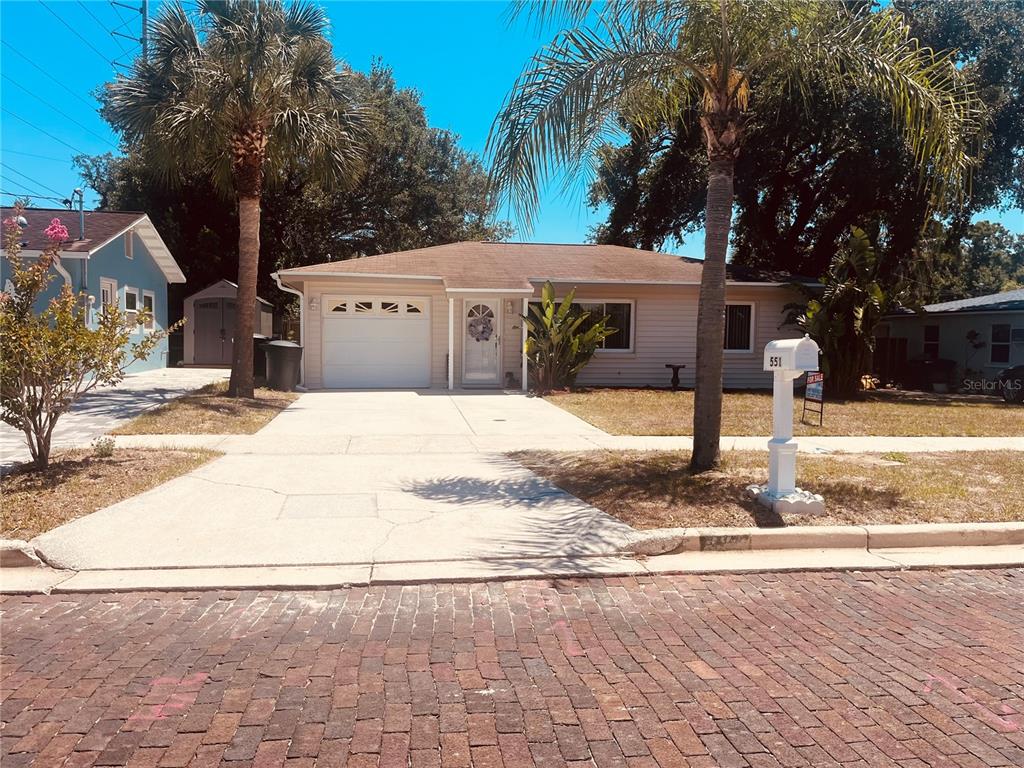 A single-story house with a beige exterior, a one-car garage, and palm trees in front — 551 ORANGEWOOD DRIVE, DUNEDIN, FL