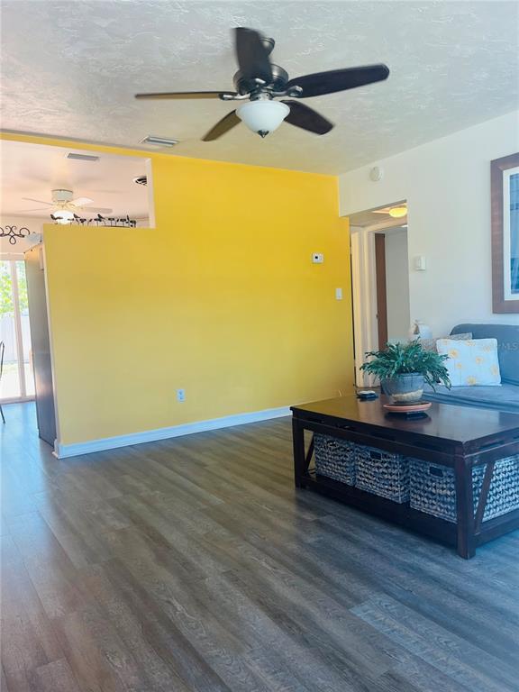 A living room features a bright yellow accent wall, wood-look flooring, and a ceiling fan — 551 ORANGEWOOD DRIVE, DUNEDIN, FL
