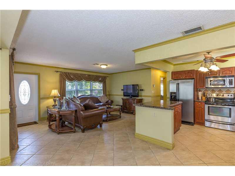 An open-concept living room and kitchen with tile floors, brown leather furniture, and stainless appliances — 160 SE 12th Street, Pompano Beach FL 33060, POMPANO BEACH, FL