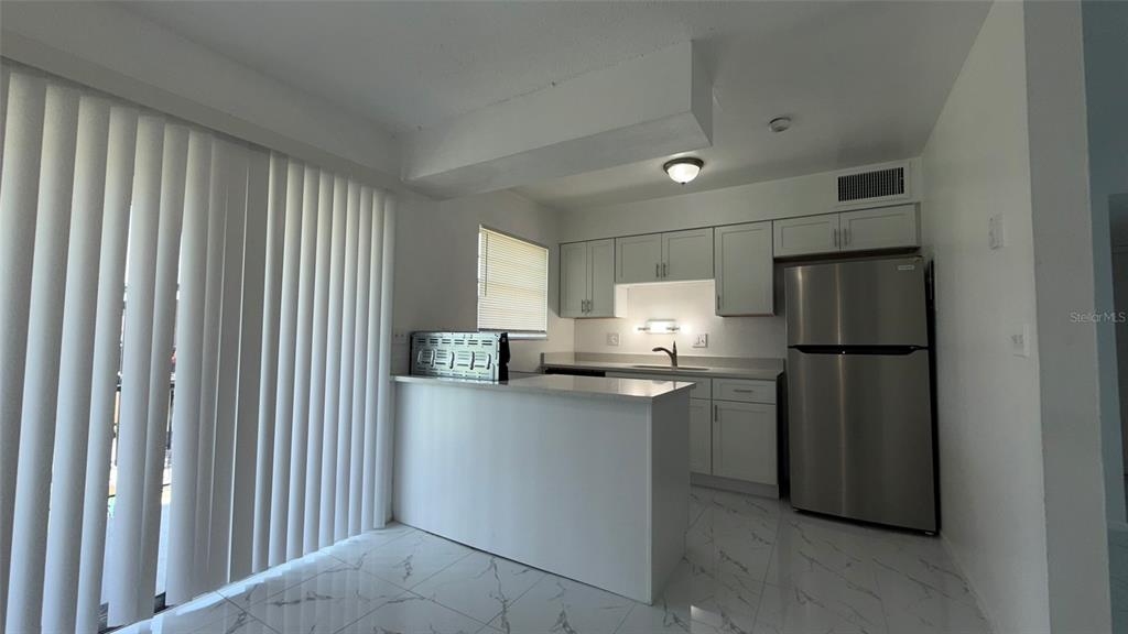 A kitchen features white cabinets, stainless steel appliances, a breakfast bar, and marble-look tile flooring — 5325 CURRY FORD ROAD UNIT D206, ORLANDO, FL