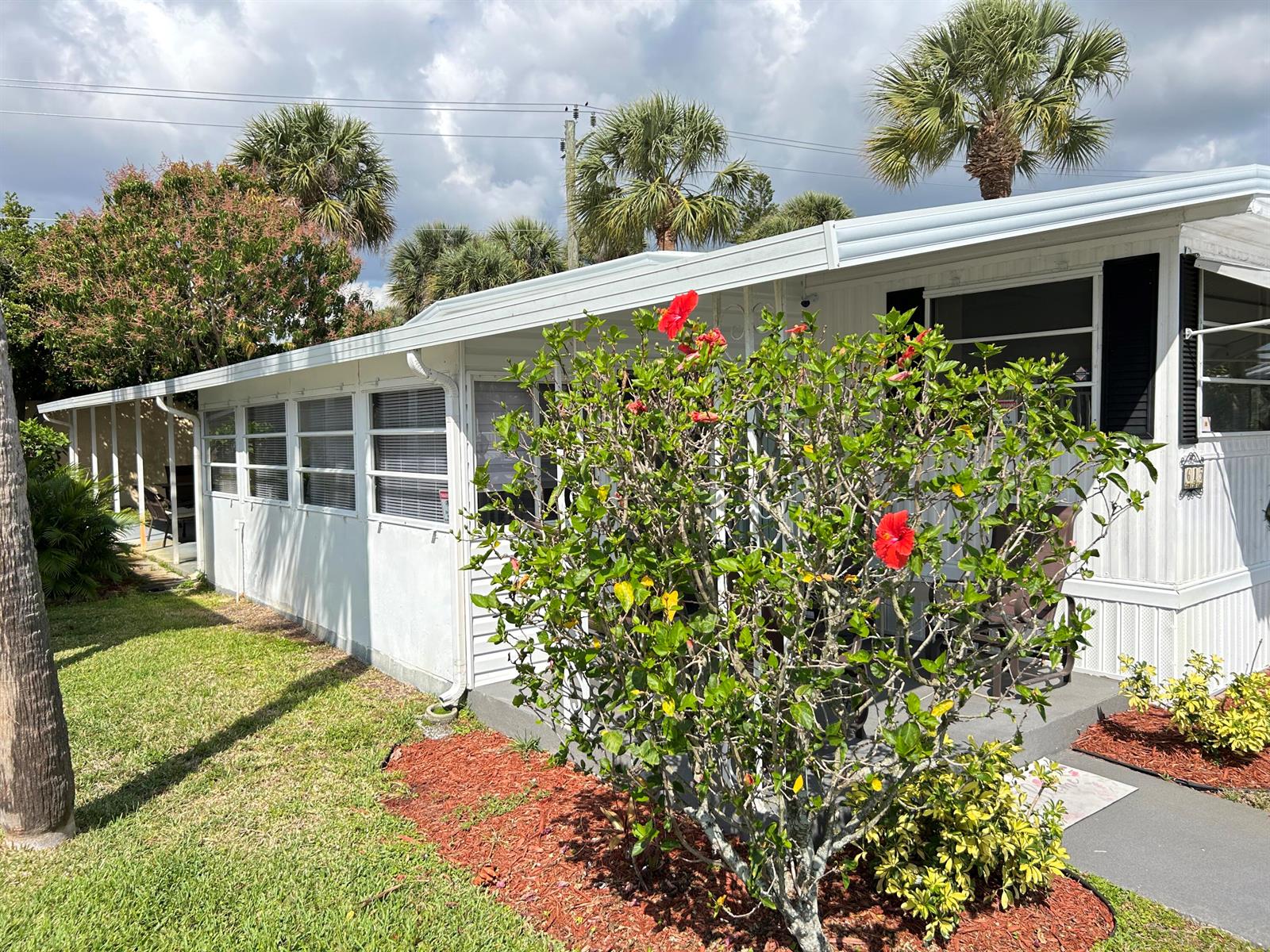 A white mobile home exterior features a screened-in porch, a hibiscus bush, and palm trees — 615 Alamanda Lane, Deerfield Beach FL 33442, DEERFIELD BEACH, FL