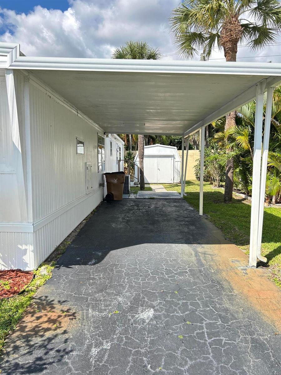 A paved carport extends from the side of a white mobile home toward a storage shed — 615 Alamanda Lane, Deerfield Beach FL 33442, DEERFIELD BEACH, FL