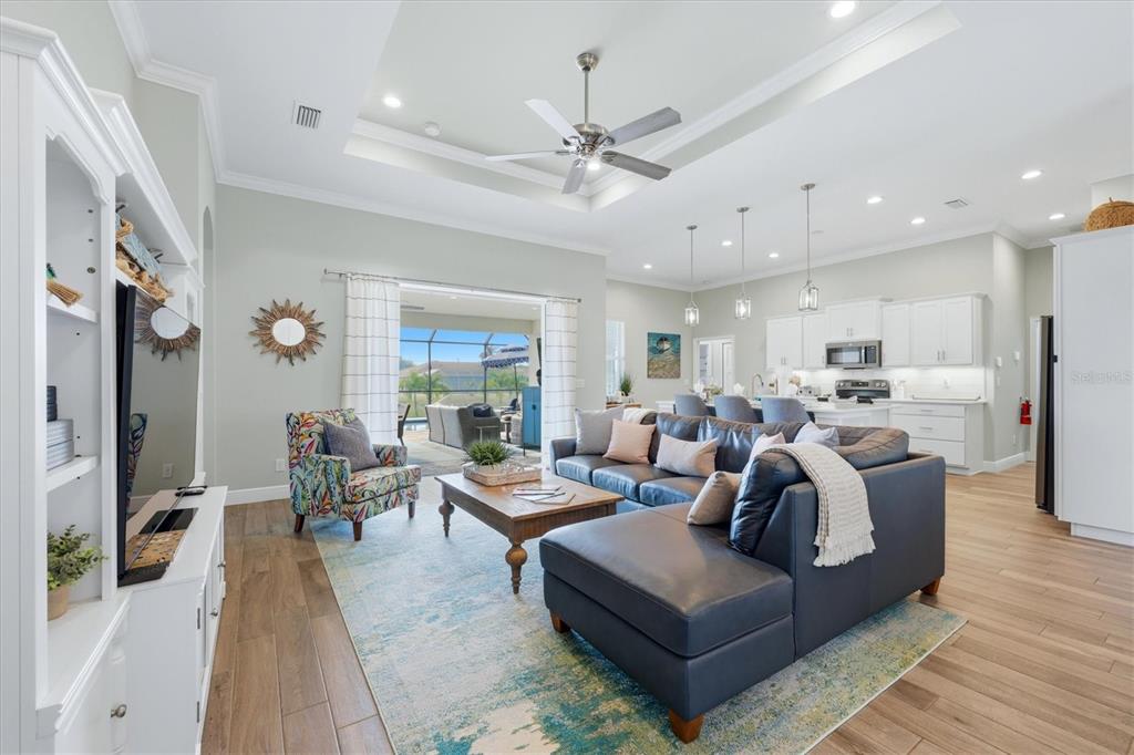 A living room with a sectional sofa, patterned armchair, and open kitchen with white cabinets — 90 BROADMOOR LANE, ROTONDA WEST, FL