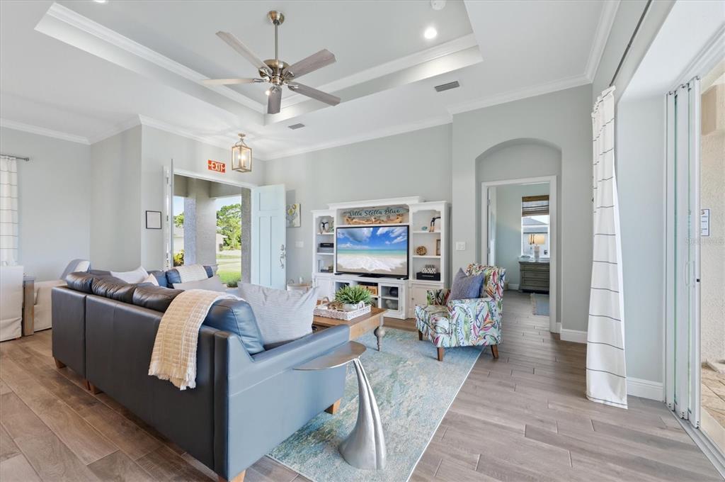 A living room features a blue sofa, patterned armchair, entertainment center, and light wood flooring — 90 BROADMOOR LANE, ROTONDA WEST, FL