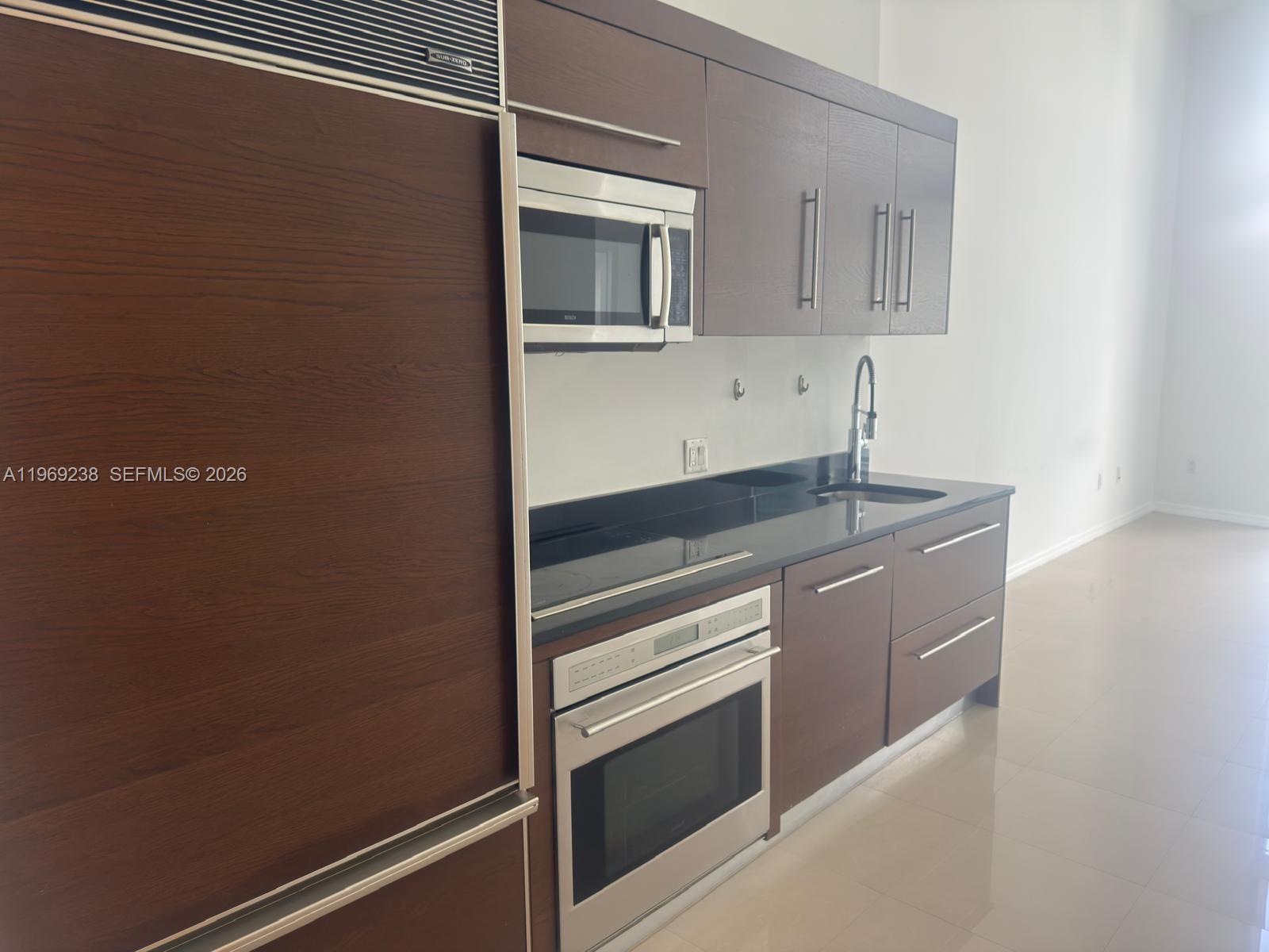 A modern kitchen features dark wood cabinetry, stainless steel appliances, and black countertops — 465 Brickell # 1504, Miami FL 33131, MIAMI, FL
