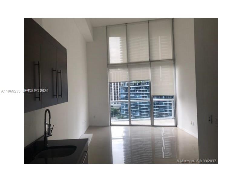 A modern kitchen area features dark cabinetry and a sink, with floor-to-ceiling windows overlooking buildings — 465 Brickell # 1504, Miami FL 33131, MIAMI, FL