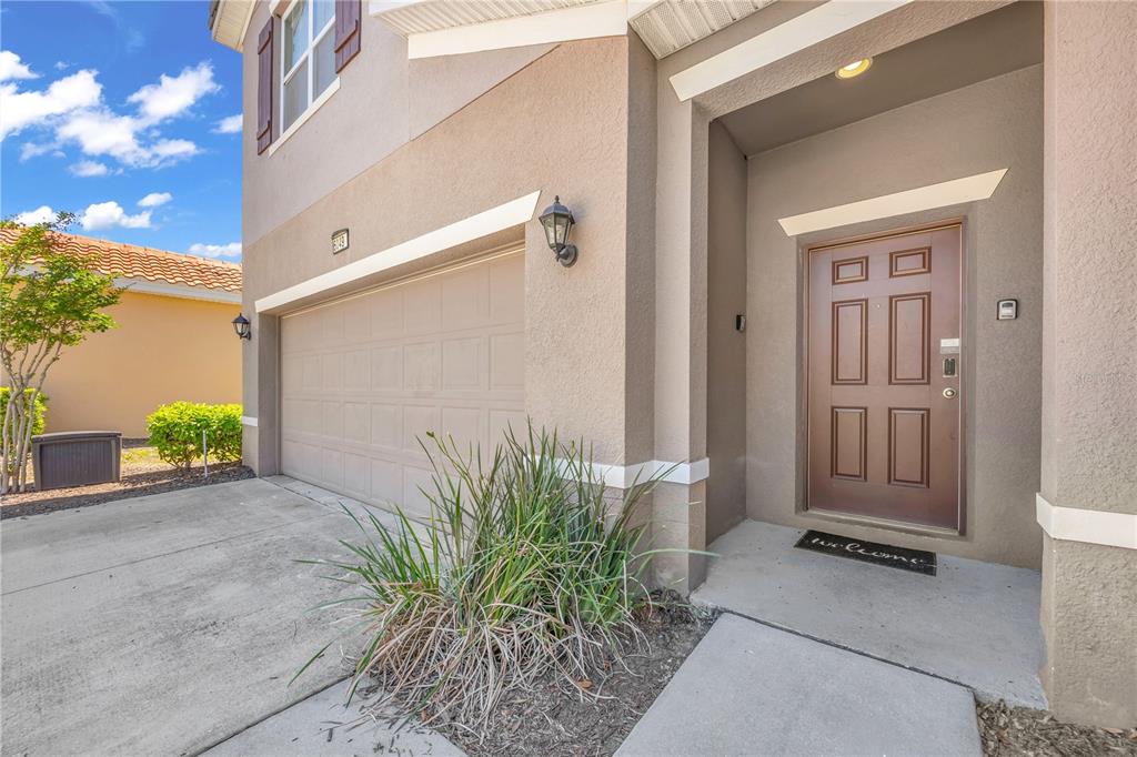 The exterior of a beige house features a two-car garage and a brown front door — 6049 BROAD OAK DRIVE, DAVENPORT, FL