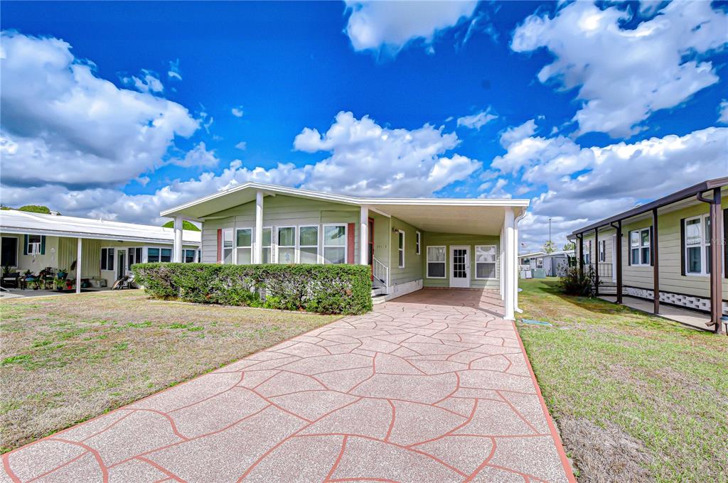 A light green mobile home features a patterned concrete driveway and a covered carport — 35145 WAGNER WAY, ZEPHYRHILLS, FL