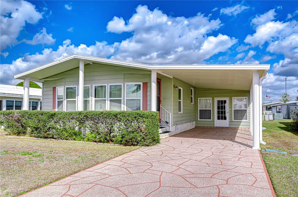 A light green manufactured home features a patterned concrete driveway and a covered carport — 35145 WAGNER WAY, ZEPHYRHILLS, FL