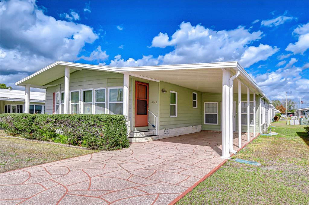 A light green manufactured home features a covered carport and a patterned concrete driveway — 35145 WAGNER WAY, ZEPHYRHILLS, FL