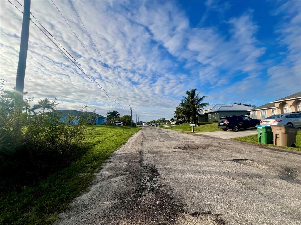 A residential street with a weathered asphalt road, parked cars, and houses under a cloudy sky — 1229 NE 13TH PLACE, CAPE CORAL, FL