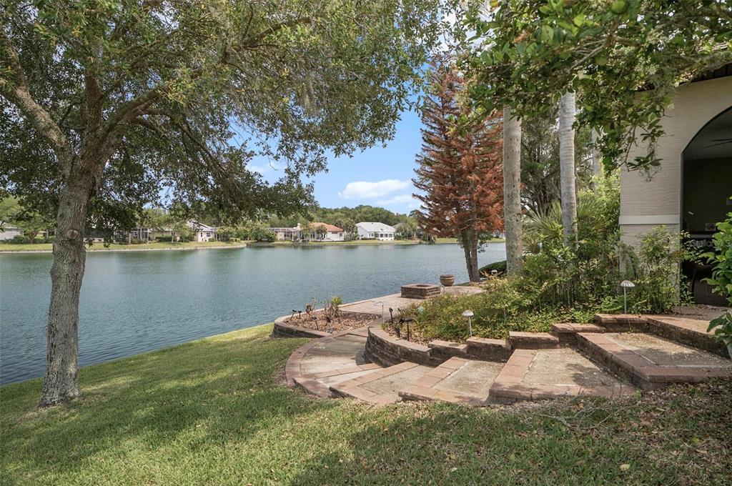 A backyard features a stone patio with a fire pit overlooking a lake — 5 SANDPIPER COURT, PALM COAST, FL