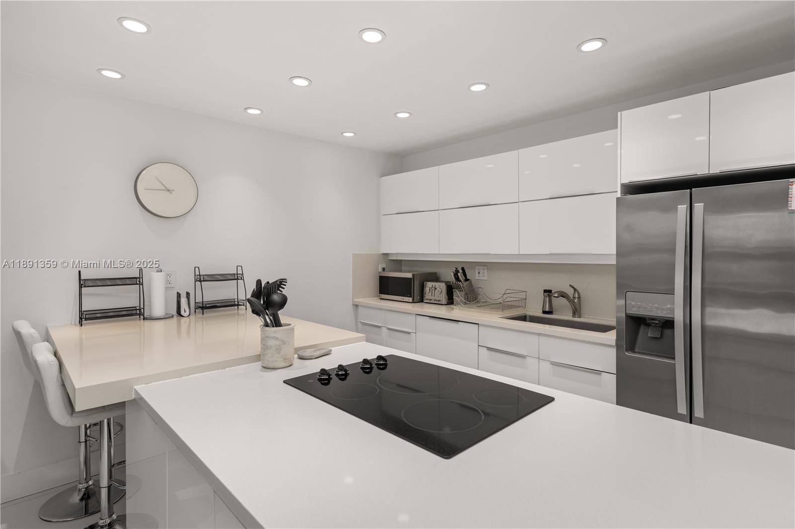 A modern kitchen features white glossy cabinets, a central island with a cooktop, and stainless-steel appliances — 101 Crandon Blvd # 379, Key Biscayne FL 33149, KEY BISCAYNE, FL
