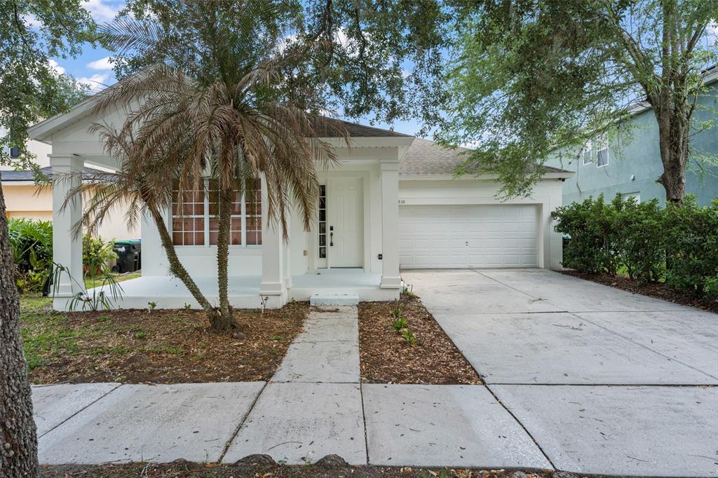 A white single-story house with a front porch, palm tree, and attached two-car garage — 8838 ABBOTSBURY DRIVE, WINDERMERE, FL