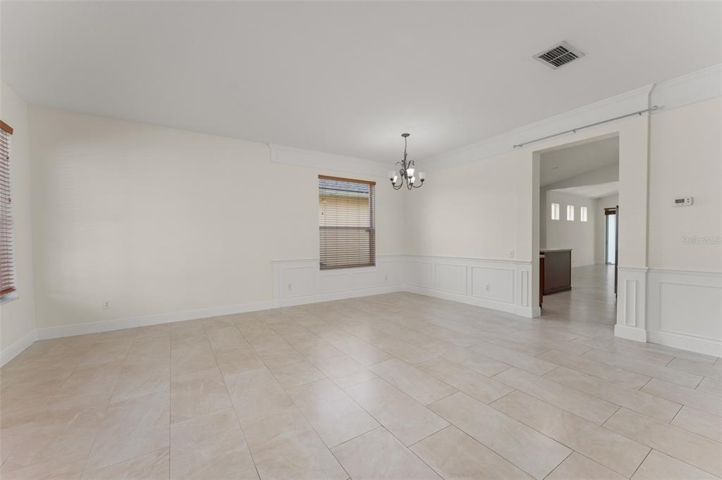 An empty dining room features tile flooring, white wainscoting, and a central chandelier — 8838 ABBOTSBURY DRIVE, WINDERMERE, FL