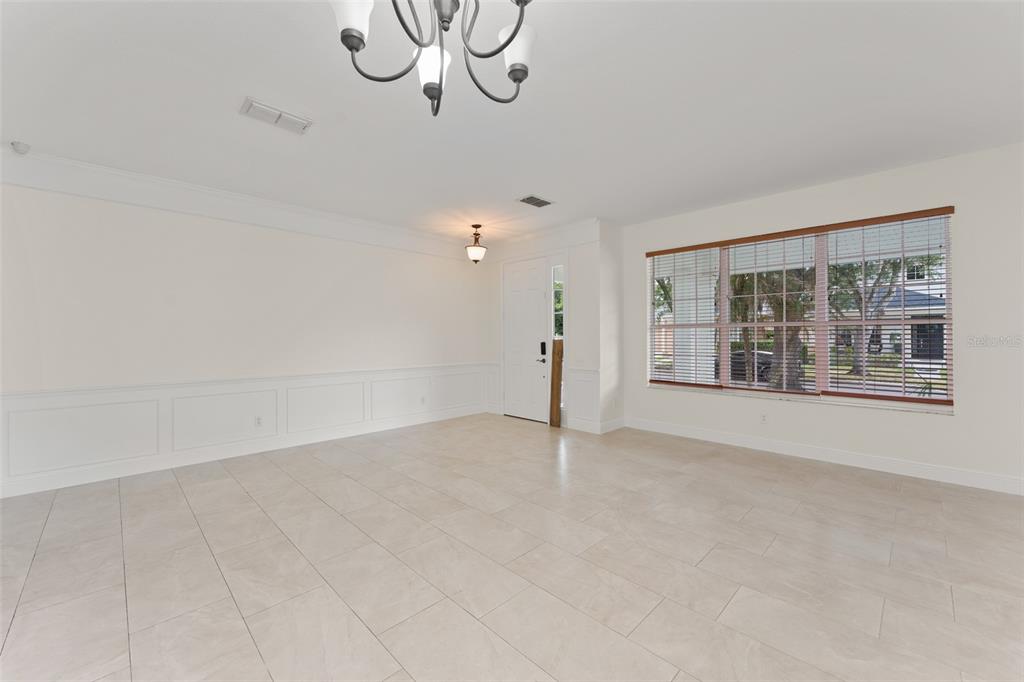A bright, empty dining room features tile floors, wainscoting, a chandelier, and large windows — 8838 ABBOTSBURY DRIVE, WINDERMERE, FL