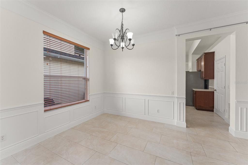 A dining room with white wainscoting, tile flooring, a chandelier, and a view into a kitchen — 8838 ABBOTSBURY DRIVE, WINDERMERE, FL