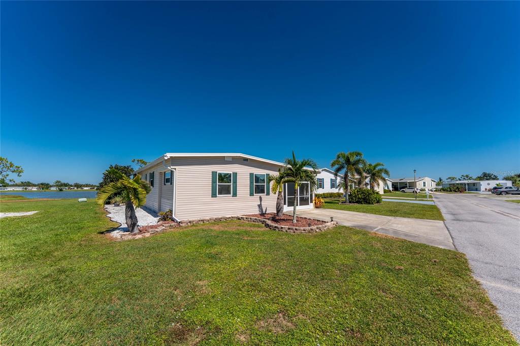 A light-colored mobile home sits on a grassy lot next to a small lake — 7548 RATAN CIRCLE, PORT CHARLOTTE, FL