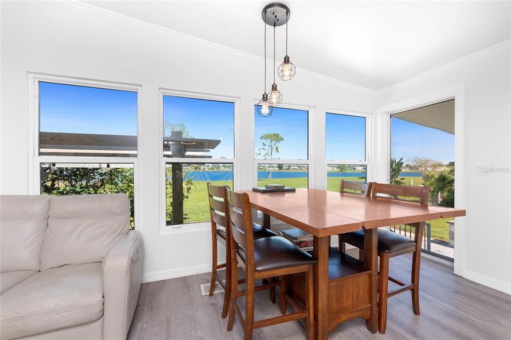 A dining area with a wooden table, chairs, pendant lights, and large windows overlooking water — 7548 RATAN CIRCLE, PORT CHARLOTTE, FL