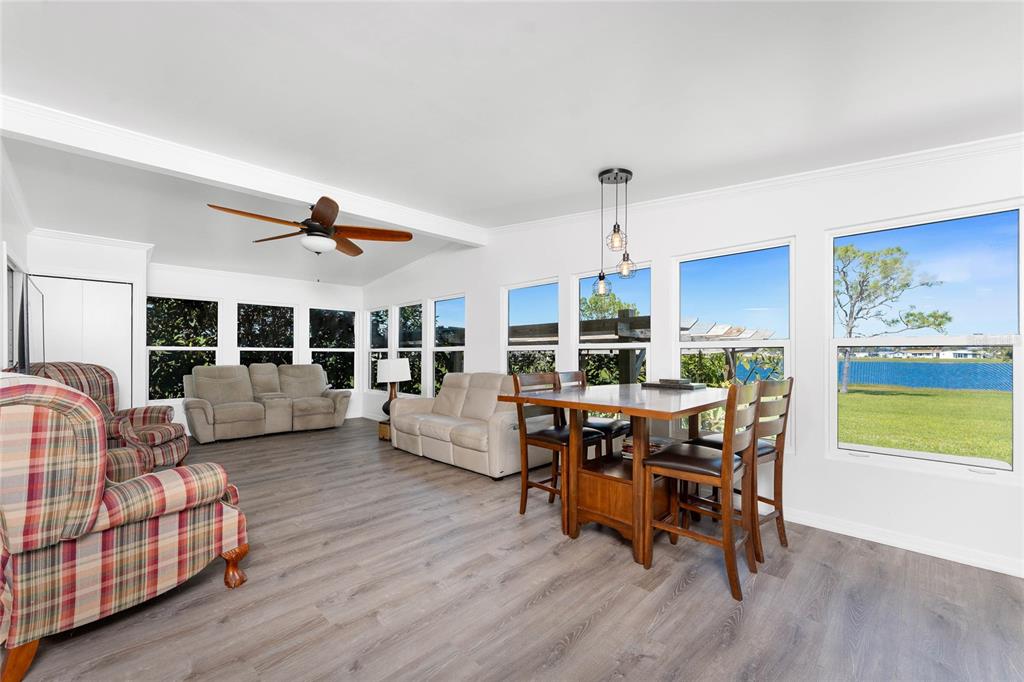 A sunroom features wood-look flooring, a dining set, seating, and large windows overlooking a lake — 7548 RATAN CIRCLE, PORT CHARLOTTE, FL