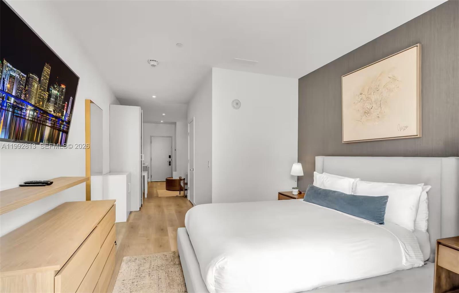 A modern bedroom features a bed, a wall-mounted television, and light wood flooring — 229 SW 9th St # 202, Miami FL 33130, MIAMI, FL