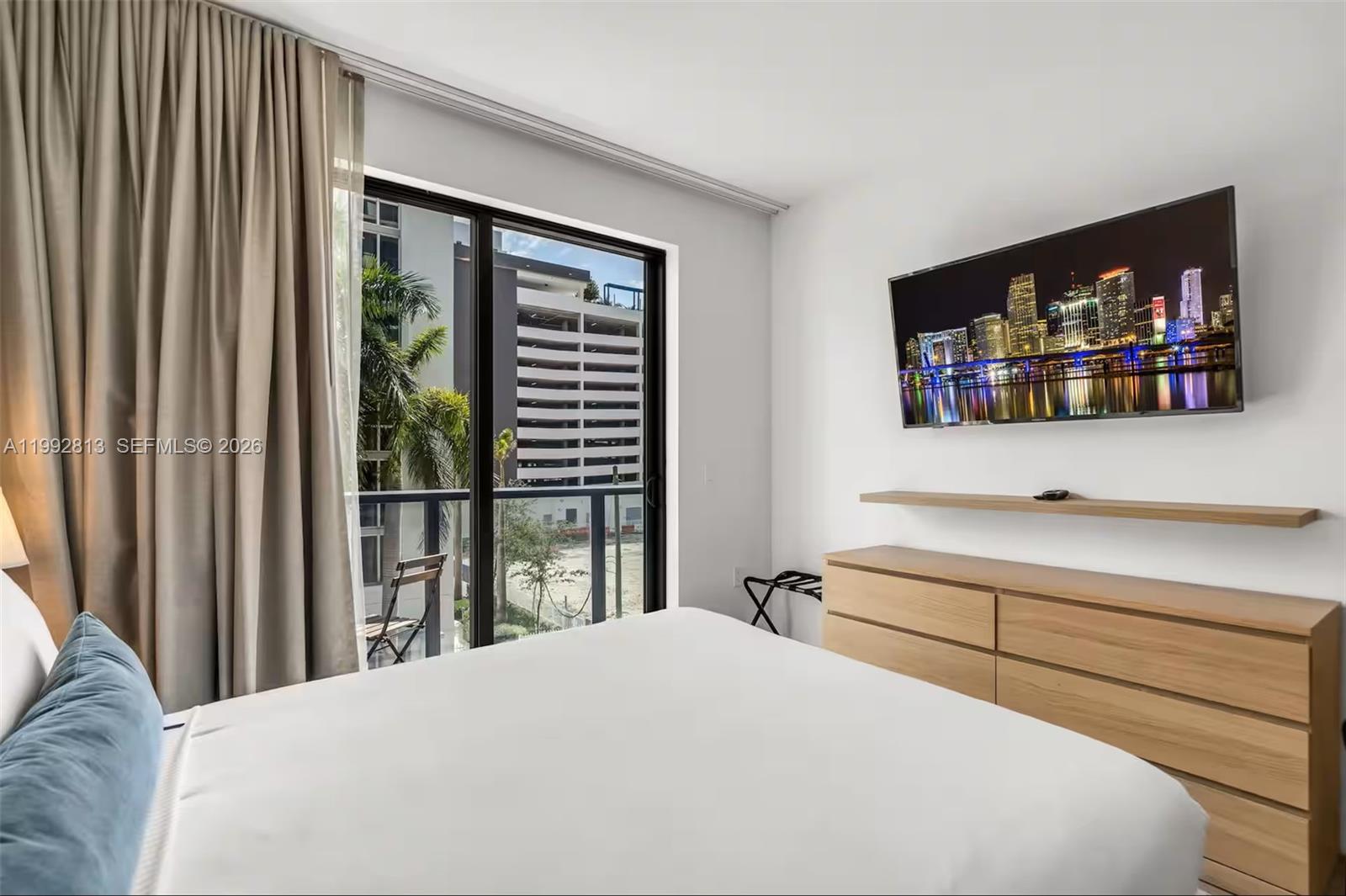 A bedroom features a bed, a wall-mounted television, a wooden dresser, and a sliding door — 229 SW 9th St # 202, Miami FL 33130, MIAMI, FL