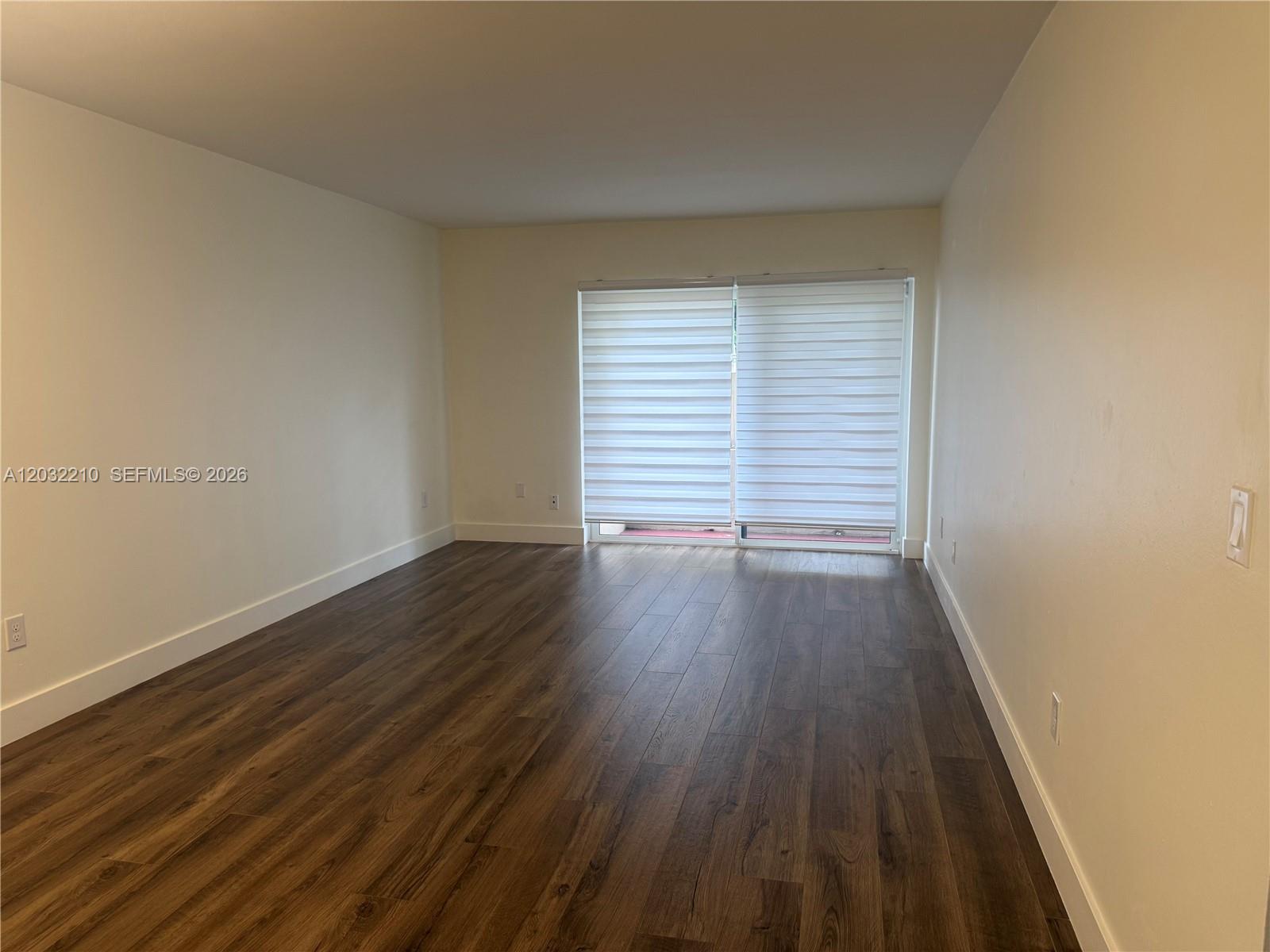 An empty room features wood-look flooring, white walls, and a sliding glass door with blinds — 7775 SW 86th St # 105, Miami FL 33143, MIAMI, FL