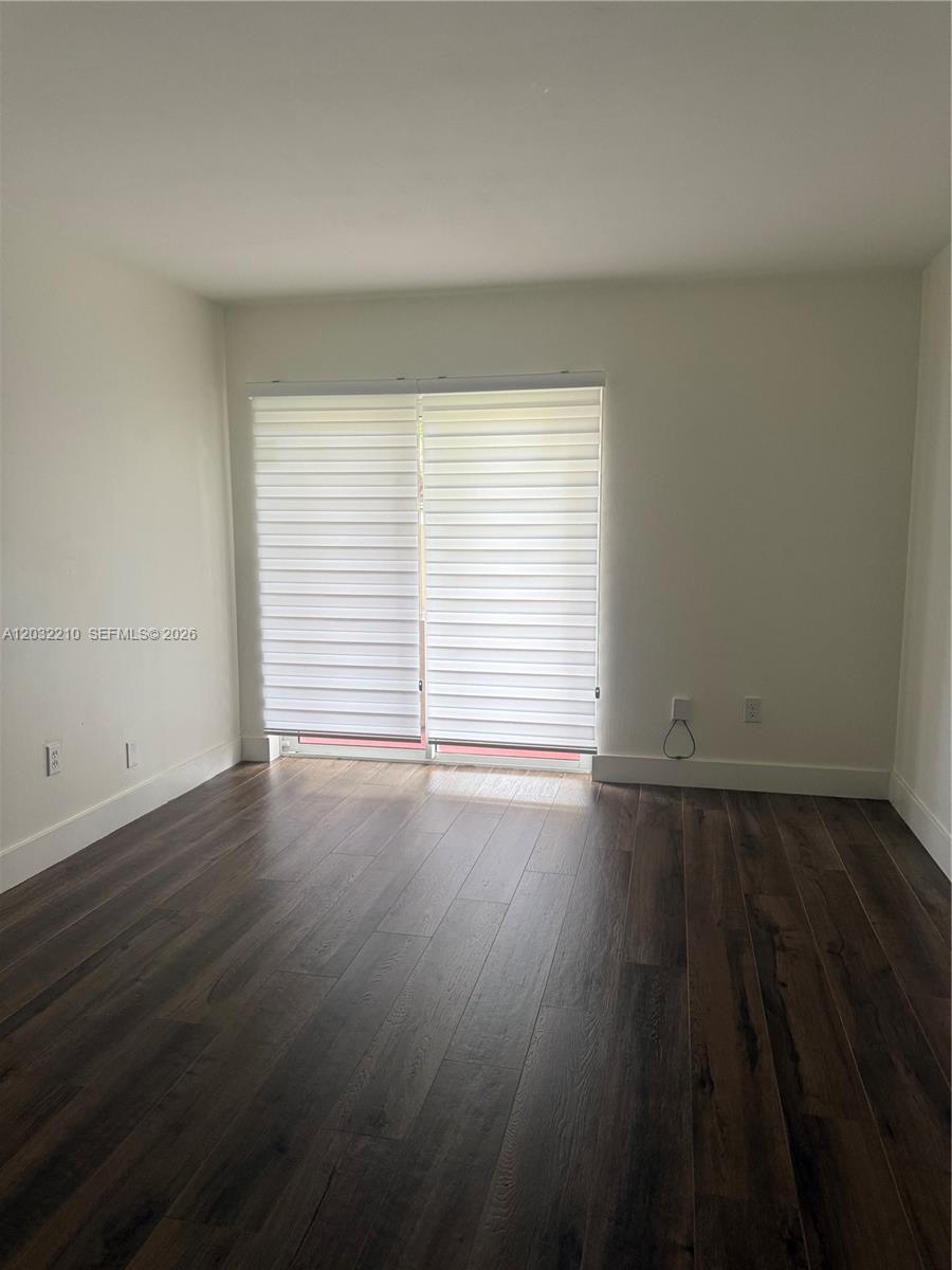 An empty room features dark wood-look flooring, white walls, and sliding glass doors with blinds — 7775 SW 86th St # 105, Miami FL 33143, MIAMI, FL