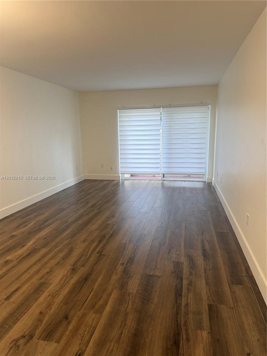 An empty room features wood-look flooring, white walls, and a sliding glass door with blinds — 7775 SW 86th St # 105, Miami FL 33143, MIAMI, FL