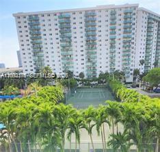An exterior view of a high-rise apartment building overlooking a tennis court and palm trees — SUNNY ISLES BEACH, FL