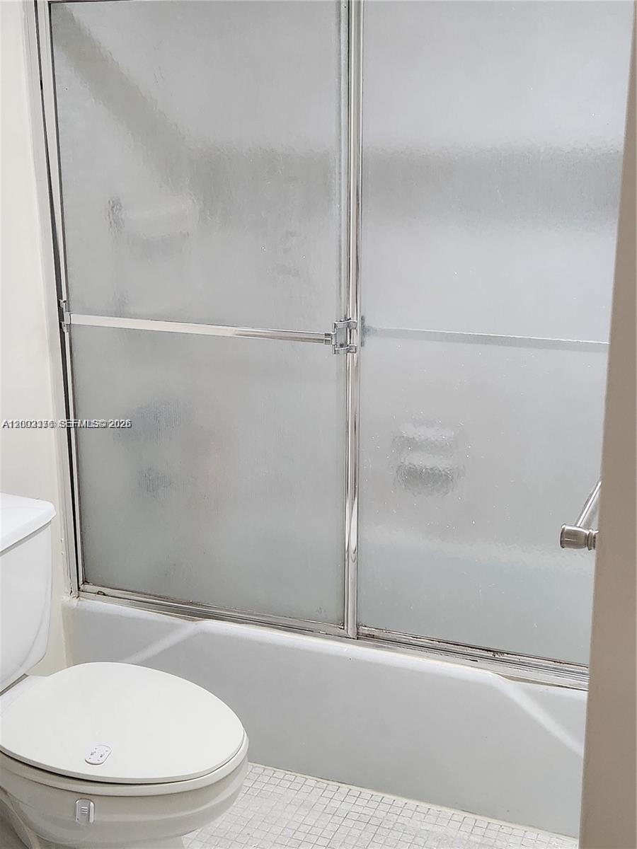 A bathroom features a white toilet next to a bathtub with sliding frosted glass doors — SUNNY ISLES BEACH, FL